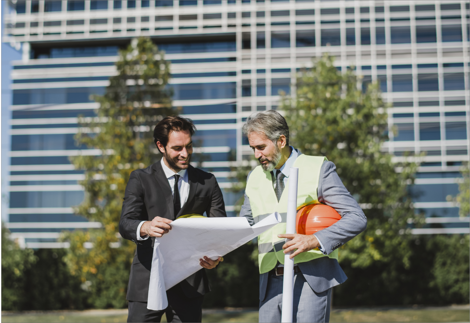 Two professionals reviewing construction plans outdoors, symbolizing how securing government contracts can drive stable business growth.