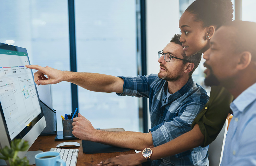 Team gathered around a computer reviewing a digital dashboard, illustrating how an eProcurement system streamlines purchasing and reduces costs.