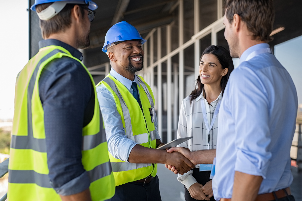 Construction and business professionals shaking hands on-site, symbolizing successful participation in public procurement and government contracting.