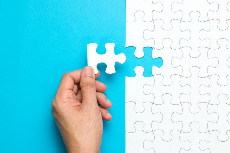Hand placing a final puzzle piece into a matching puzzle, symbolizing Ontario’s partnership with bids&tenders for seamless procurement integration.