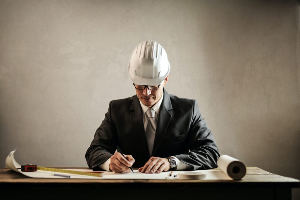 Architect or construction professional in a suit and hard hat reviewing plans at a desk, symbolizing getting started with creating an account and beginning to bid.
