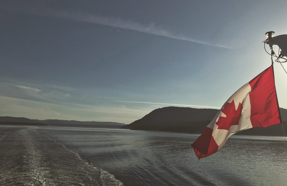 Canadian flag flying over open water at sunset, symbolizing Canada’s trade treaty obligations and their impact on procurement compliance.